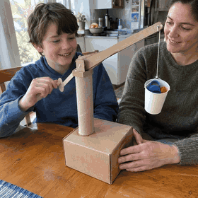 A child presses down the arm of a craft stick catapult next to a sketch of it